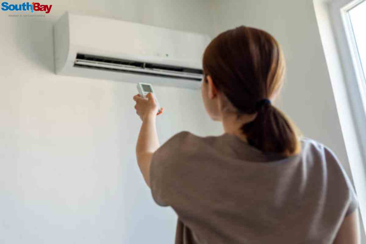A woman holds a remote control, adjusting the air conditioner to improve AC performance and fix AC problems caused by high temperatures in a modern living room.