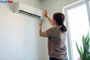 A woman is cleaning an air conditioner to prevent AC problems caused by high temperatures and maintain optimal AC performance during summer.