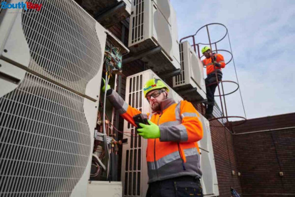 Two technicians performing emergency AC repair on a large air conditioning system in an industrial environment.