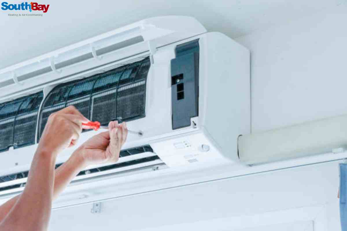 A technician performing garage AC repair by adjusting the air conditioner and fixing its mechanical components.