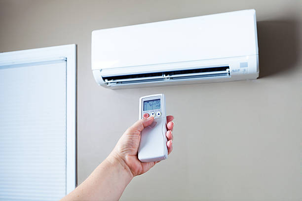 A person holding a remote control, looking concerned in front of an air conditioner displaying an "AC Not Cooling" message.