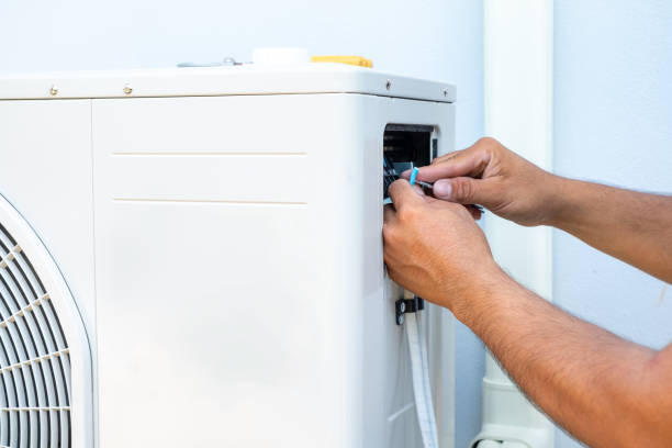 A man performs compressor repair on a heat pump inside a room, carefully focused on fixing the unit's internal components to restore proper cooling and heating function.