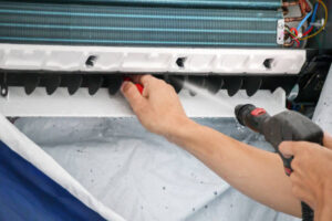  A man in gloves is cleaning the coils of an air conditioner, focusing on maintenance and repair. 