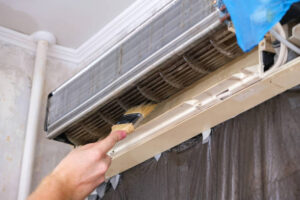  A person cleaning an air conditioner with a brush, demonstrating proper maintenance of AC systems. 