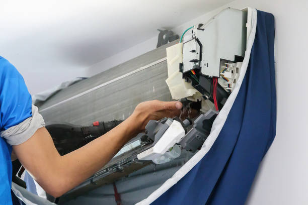 A man is repairing an air conditioner, focusing on the Maintenance of AC Systems to ensure proper functionality and long-term performance.
