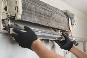A technician engaged in air conditioner maintenance, specifically cleaning the AC coils to enhance cooling efficiency.